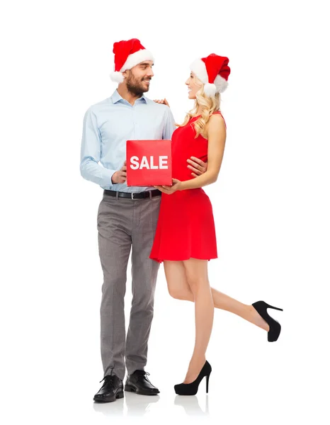 Heureux couple dans santa chapeaux avec signe de vente rouge — Photo