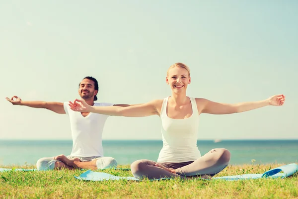 Pareja sonriente haciendo ejercicios de yoga al aire libre —  Fotos de Stock