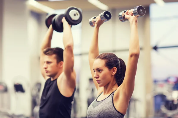 Sonriente hombre y mujer con mancuernas en el gimnasio —  Fotos de Stock