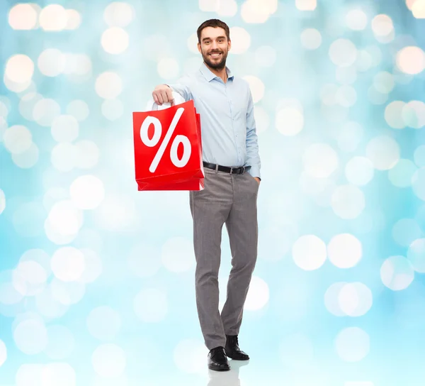 Homem sorridente com saco de compras vermelho sobre luzes azuis — Fotografia de Stock