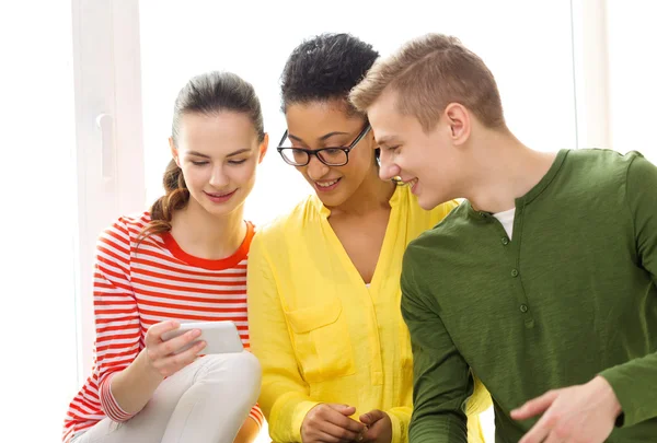 Tre studenti sorridenti con smartphone a scuola — Foto Stock