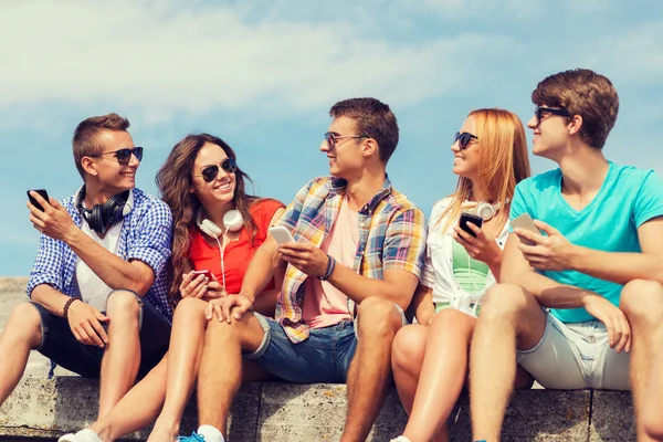 Grupo de amigos sonrientes con teléfonos inteligentes al aire libre — Foto de Stock