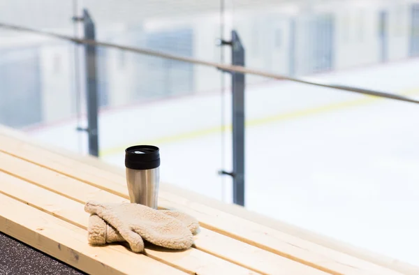 Thermos cup and mittens on bench at ice rink arena — Stock fotografie