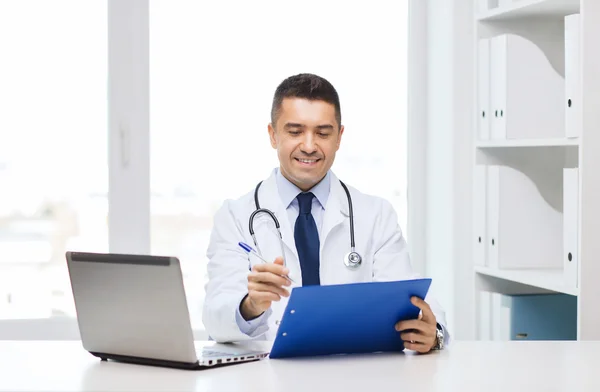 Médecin heureux avec presse-papiers et ordinateur portable au bureau — Photo