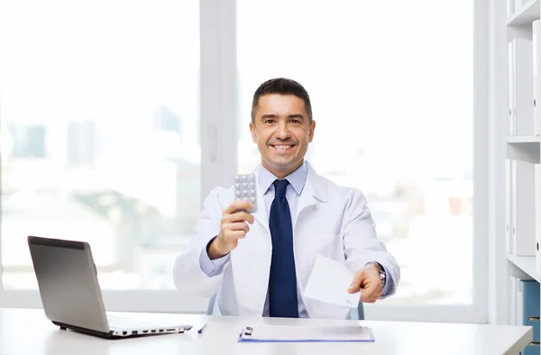 Médecin souriant avec des comprimés et un ordinateur portable au bureau — Photo