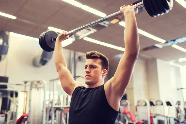 Jovem homem flexionando músculos com barbell no ginásio — Fotografia de Stock