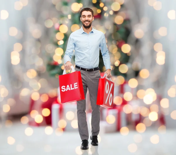 Glücklicher Mann mit Einkaufstüten über Weihnachtsbeleuchtung — Stockfoto