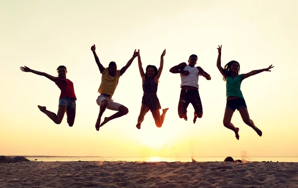 Amigos sonrientes bailando y saltando en la playa — Foto de Stock