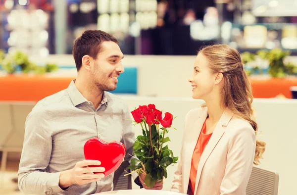 Happy couple with present and flowers in mall — Stock Photo, Image