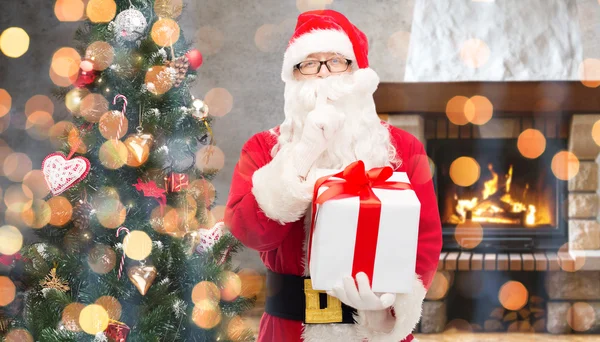 Santa claus with gift making hush gesture at home — Stok fotoğraf