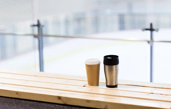 Coffee and thermos cup on bench at ice rink arena — Stock Photo, Image