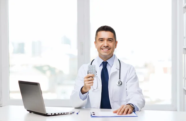 Médico sonriente con tabletas y portátil en la oficina —  Fotos de Stock