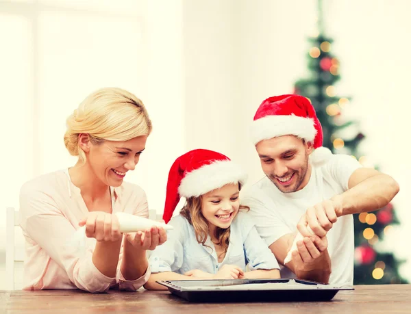 Happy family in santa helper hats making cookies — Stock Photo, Image