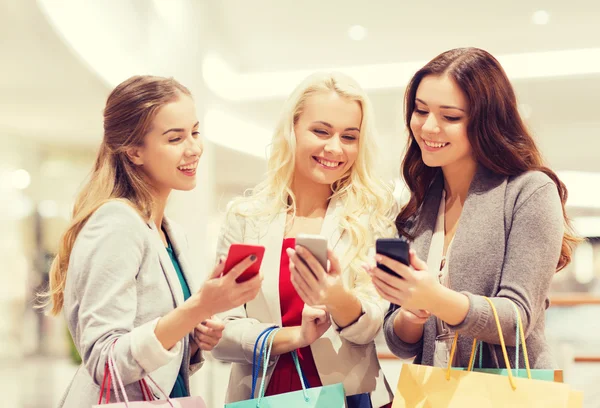 Glada kvinnor med smartphones och påsar — Stockfoto