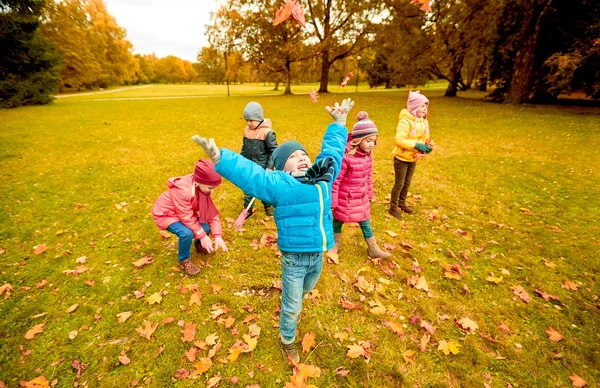 Glückliche Kinder spielen mit Herbstblättern im Park — Stockfoto