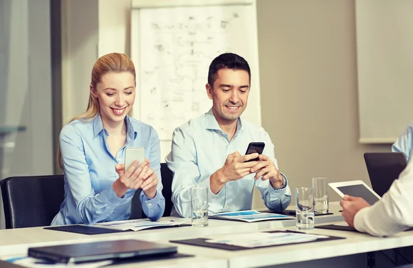 Uomini d'affari sorridenti con smartphone in ufficio — Foto Stock