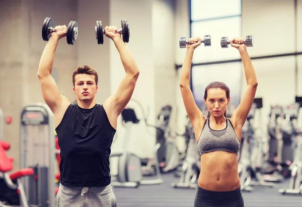 Sonriente hombre y mujer con mancuernas en el gimnasio —  Fotos de Stock