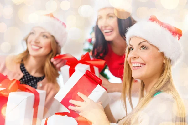 Happy women in santa hats with christmas gifts — Stock Photo, Image