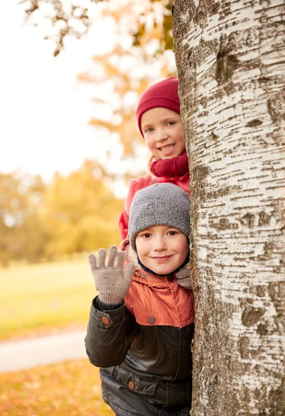 Happy children hiding behind tree and waving hand — Stock Photo, Image