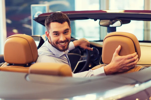 Homem feliz sentado no carro no auto show ou salão — Fotografia de Stock