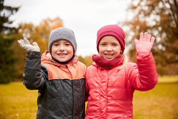 Happy girl and boy waving hands in autumn park — Stockfoto