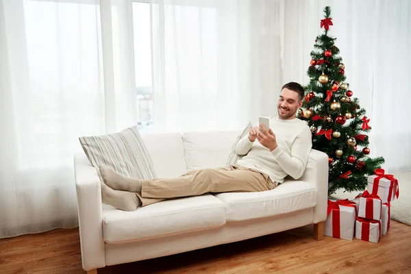 Glimlachende man met smartphone thuis voor Kerstmis — Stockfoto