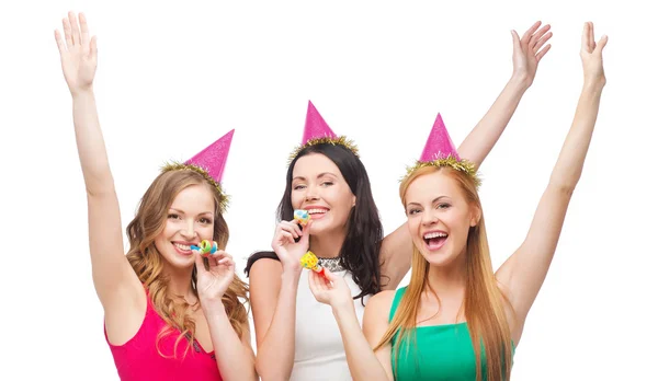 Tre leende kvinnor i hatt blåser gunst horn — Stockfoto