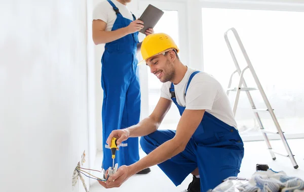 Builders with tablet pc and fixing wiring indoors — Stock Photo, Image