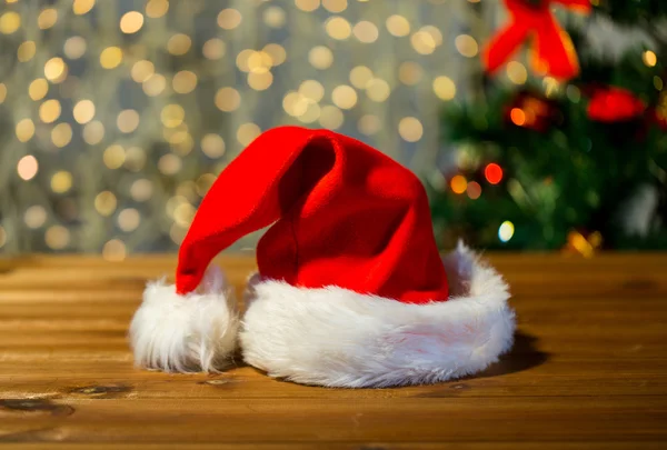 Close up of santa hat on wooden table over lights — Stock Photo, Image