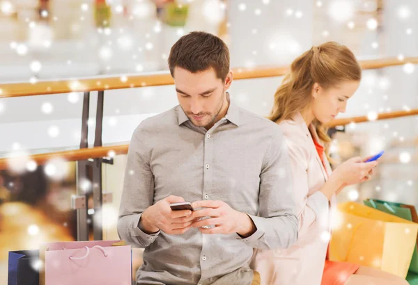 Pareja con smartphones y bolsas de compras en el centro comercial —  Fotos de Stock