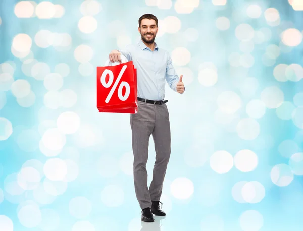 Uomo sorridente con la shopping bag rossa sopra le luci blu — Foto Stock
