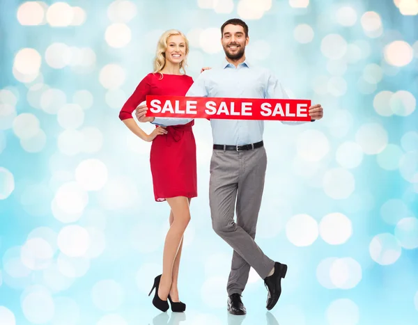 Happy couple with red sale sign over blue lights — Stock Fotó