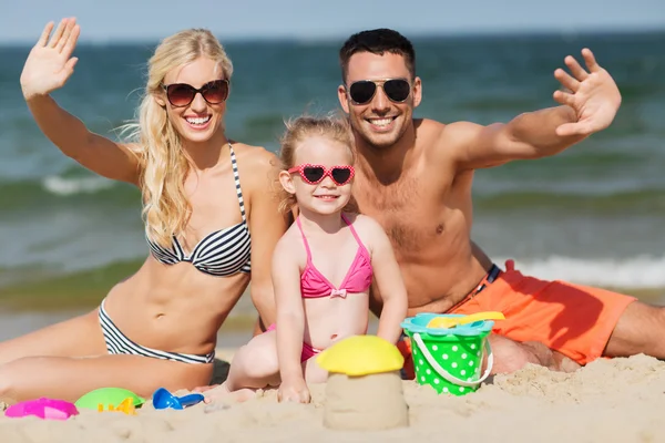 Familia feliz con juguetes de arena agitando las manos en la playa — Foto de Stock