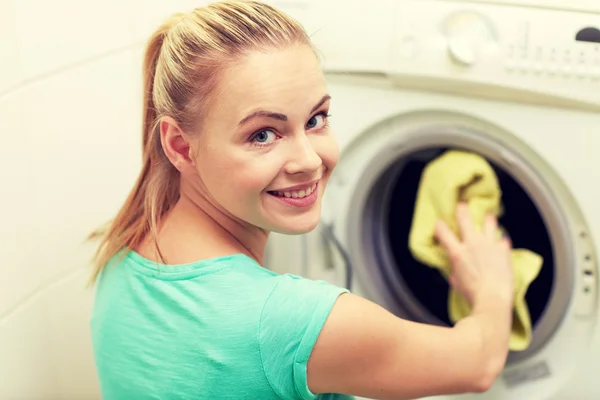 Mujer feliz poniendo la ropa en la lavadora en casa —  Fotos de Stock