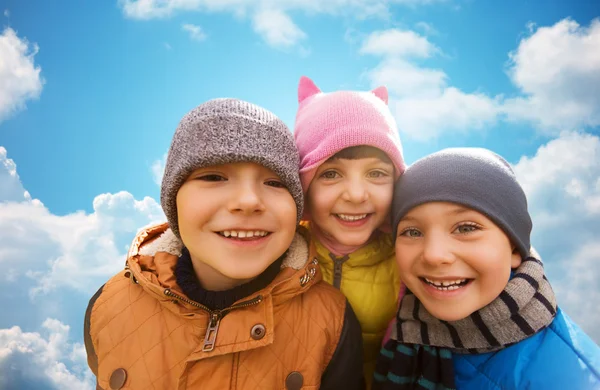 Happy children hugging over blue sky background — Stock Photo, Image