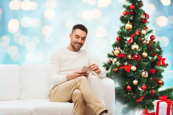 Hombre sonriente con teléfono inteligente sobre luces de Navidad —  Fotos de Stock