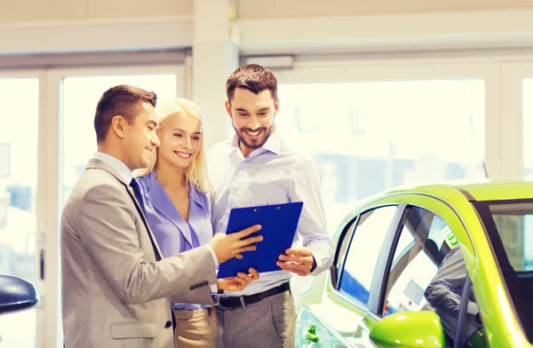 Casal feliz com revendedor de carro em auto show ou salão — Fotografia de Stock