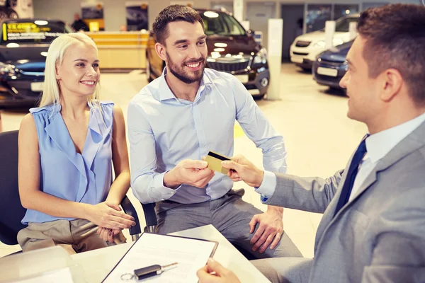 Glückliches Paar mit Autohändler in Auto-Show oder Salon — Stockfoto