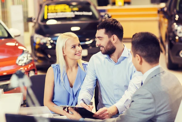 Couple heureux avec concessionnaire de voitures en salon ou salon de l'auto Images De Stock Libres De Droits