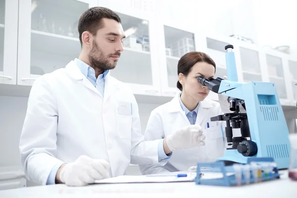 Cientistas com área de transferência e microscópio em laboratório — Fotografia de Stock