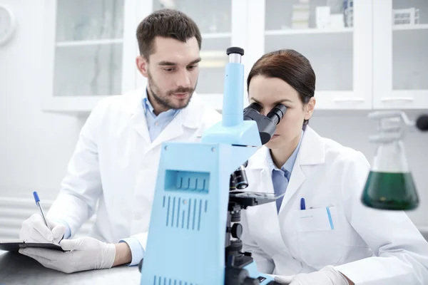 Wetenschappers met Klembord en Microscoop in lab — Stockfoto