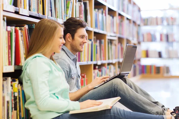 Счастливые студенты с ноутбуком в библиотеке — стоковое фото