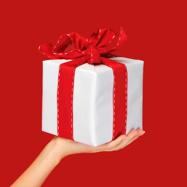 Close up hand holding christmas gift box over red — Stok fotoğraf