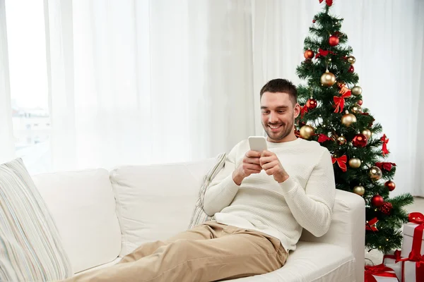 Lächelnder Mann mit Smartphone zu Weihnachten zu Hause — Stockfoto