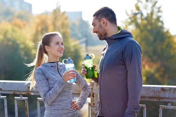 Casal sorrindo com garrafas de água ao ar livre — Fotografia de Stock