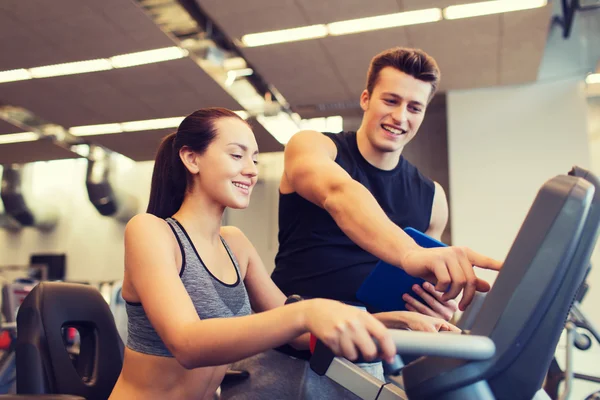 Spor salonunda egzersiz bisikleti üzerinde eğitmen ile mutlu kadın — Stok fotoğraf