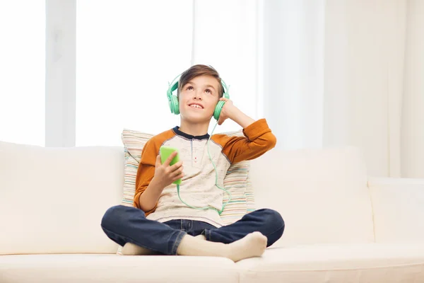 Niño feliz con teléfono inteligente y auriculares en casa —  Fotos de Stock