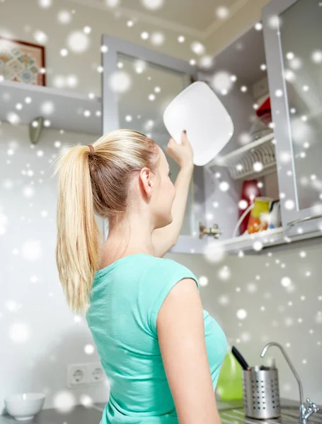 Mulher feliz colocando prato para armário de cozinha — Fotografia de Stock