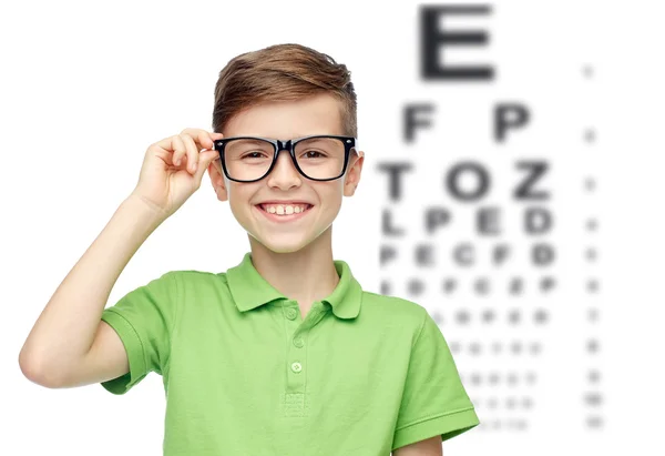 Happy boy in eyeglasses over eye chart — Stock Photo, Image