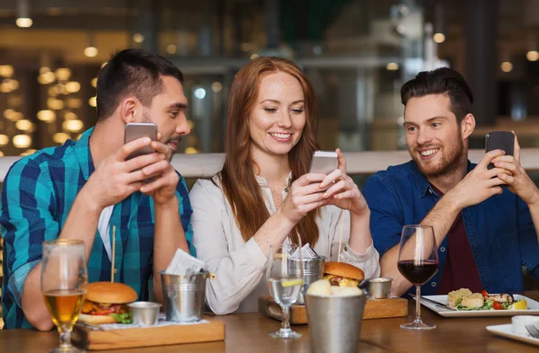 Glada vänner med smartphones på restaurang — Stockfoto